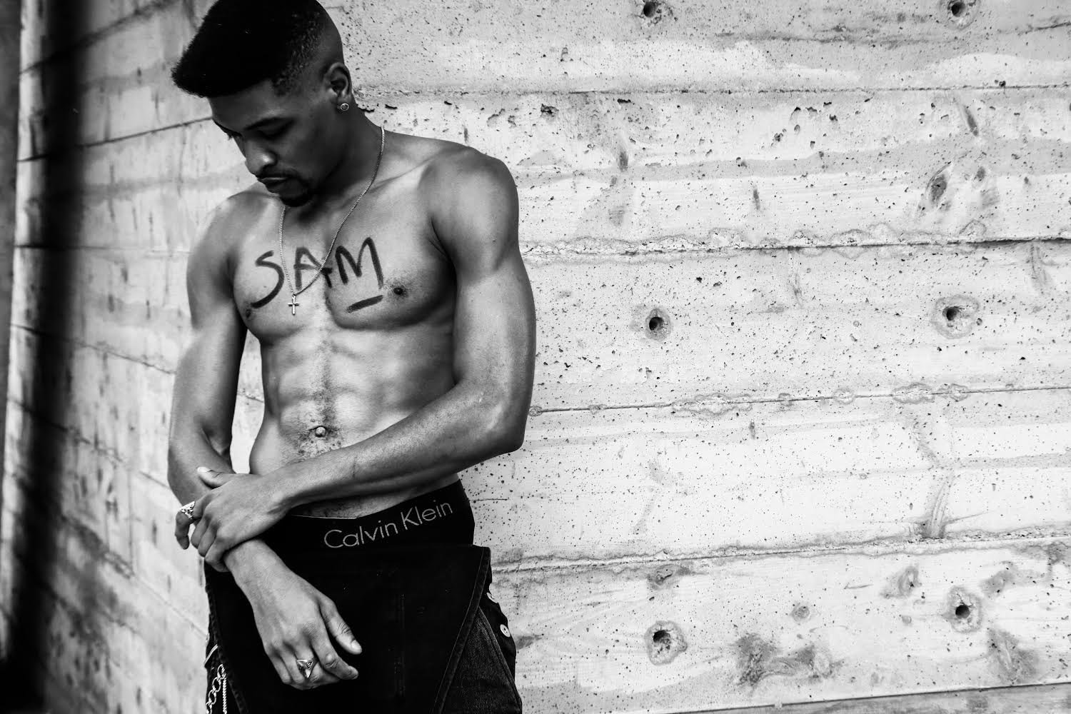 Black-and-white modeling portrait of Sam beside a brick wall