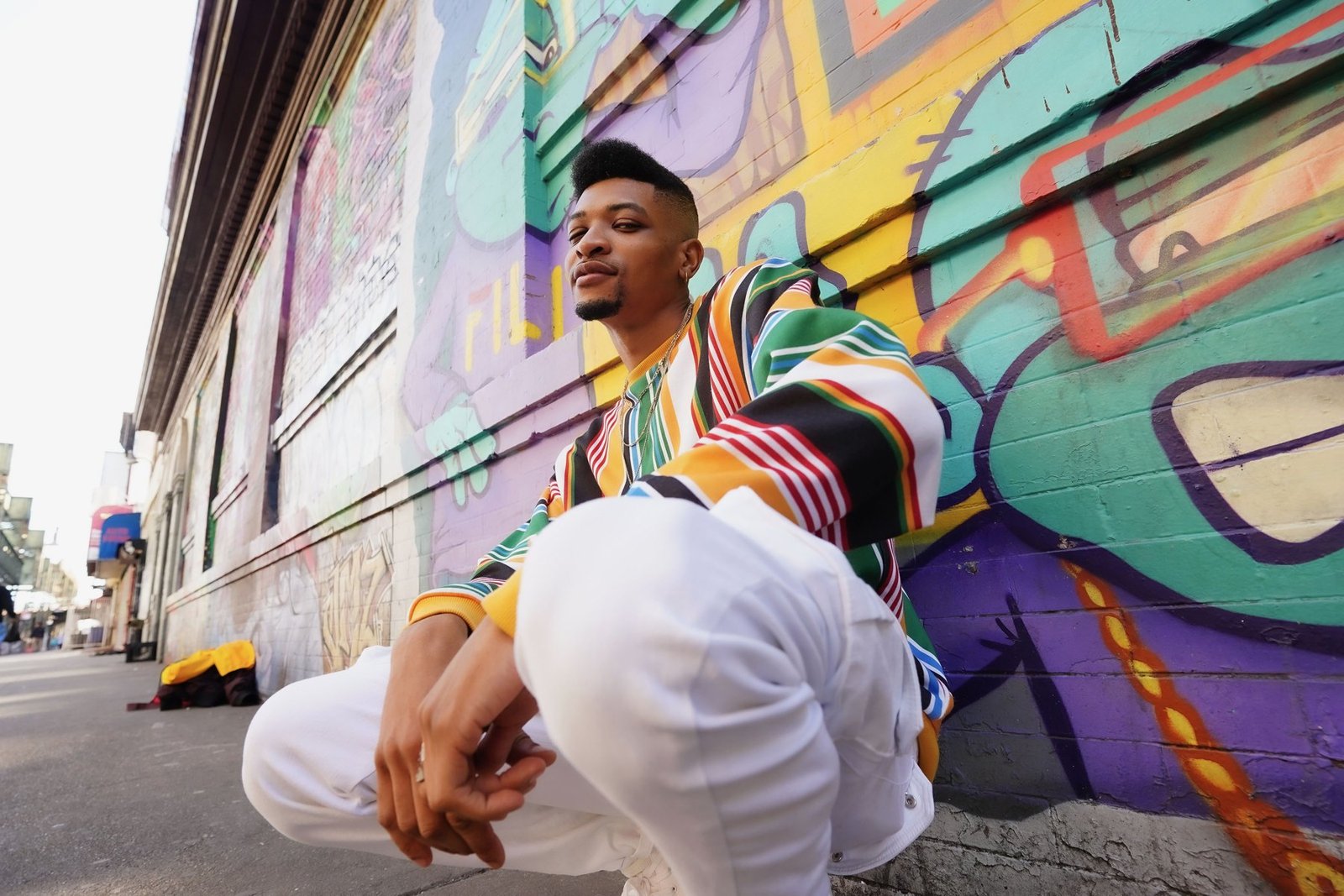 Sam in colorful streetwear beside a graffiti mural